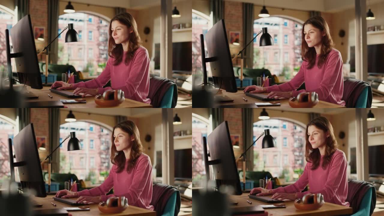 穿着粉色套头衫的年轻漂亮女性在家用台式电脑工作。有创造力的女人检查社交媒体，浏览互联网。阁楼公寓，从