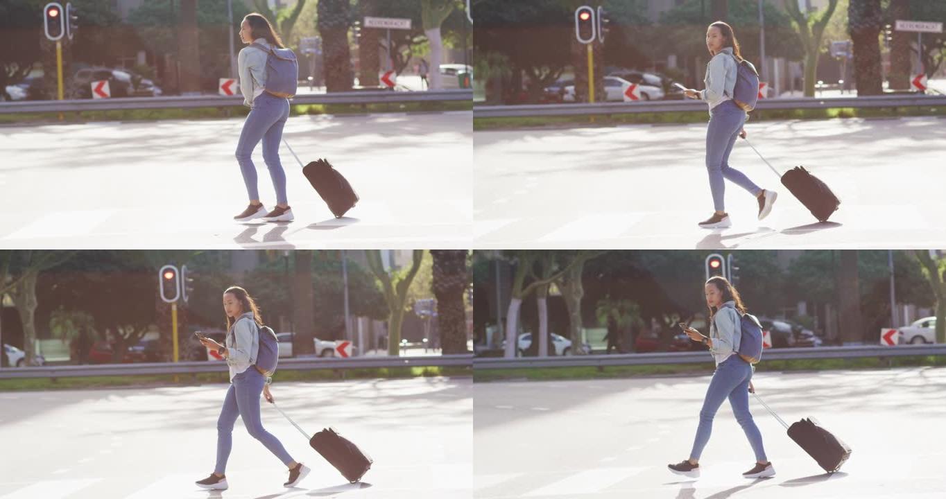 亚洲妇女使用智能手机行走并拖着手提箱
