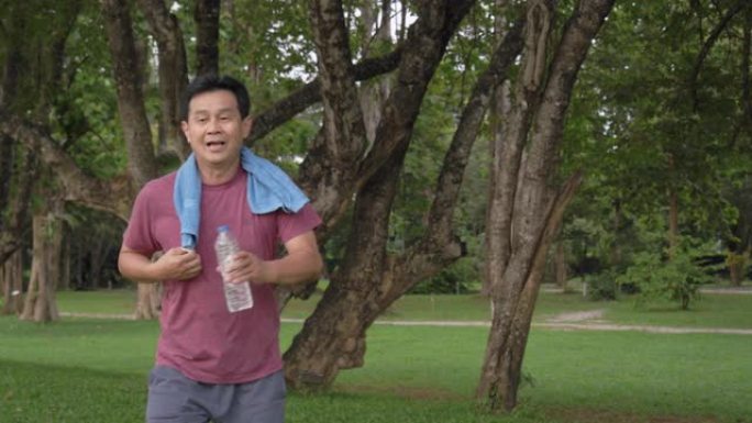 手持镜头: 亚洲高级男子早上在公园跑步后休息。他用毛巾擦干锻炼时的汗水。做瑜伽和太极拳运动后，他累了