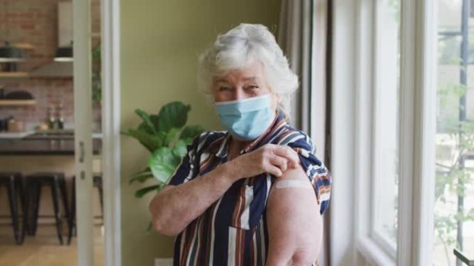 戴着口罩的白人高级妇女在家里展示了接种疫苗的肩膀
