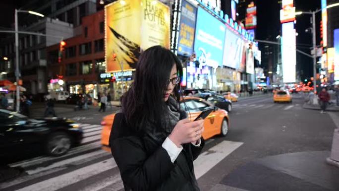 亚洲女子夜间在时代广场使用智能手机