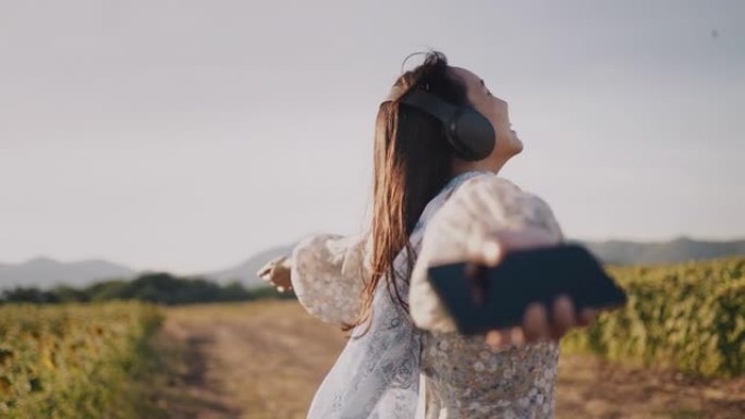 自由女人张开双臂，用智能手机和耳机欣赏音乐