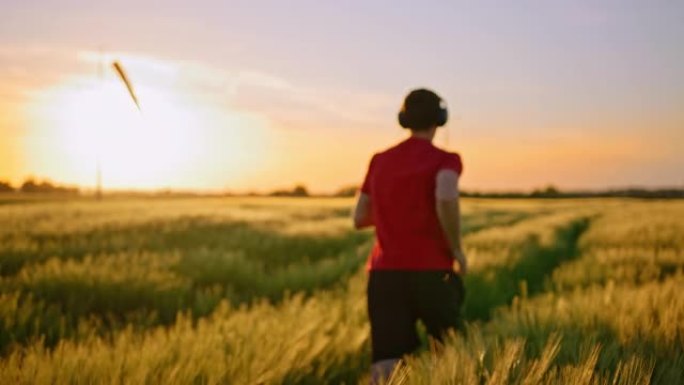 男运动员的慢动作镜头在草地上开始跑步，播放音乐并奔向日落