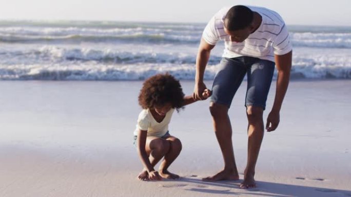 非洲裔美国父女在海滩上一起从沙子上捡起贝壳