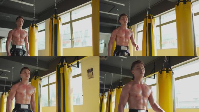 亚洲华裔男运动员在健身房健身俱乐部散步，一排黄色沙袋在窗口旁边