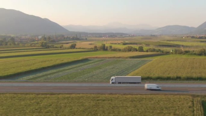 空中: 沿着一辆白色半卡车飞行，沿着风景秀丽的高速公路拖运货物。