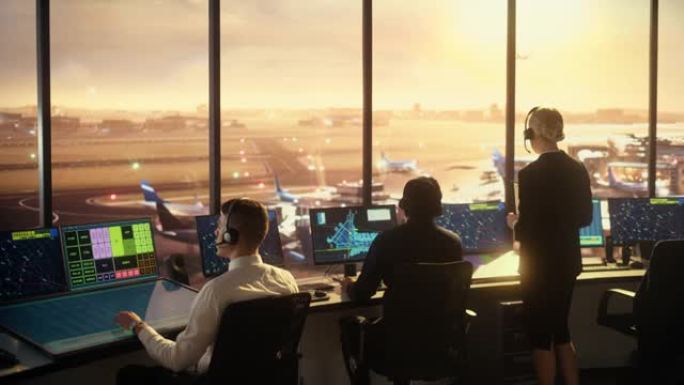 日落时在现代机场塔中工作的多元化空中交通管制团队。办公室里满是台式电脑显示屏，配有导航屏幕，飞机飞行