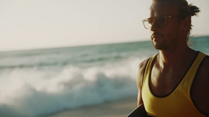 成年男子在海滩上散步，在日落时手臂下背着冲浪板