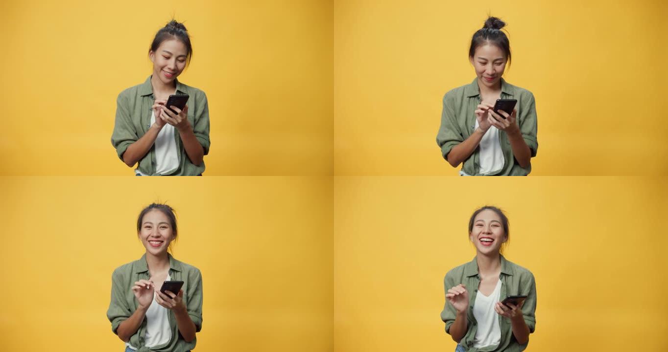 迷人的亚洲青年孤立女士在空旷的空间玩智能手机感到无聊的思考发送信息情感和快乐的微笑看着黄色背景上的相