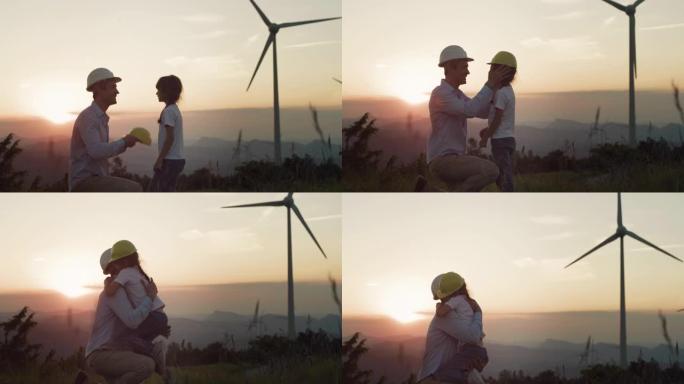 日落中的风电场: 男工程师在女儿的头上戴上防护头盔，拥抱她，给孩子们应有的清洁未来。父亲确保孩子对可