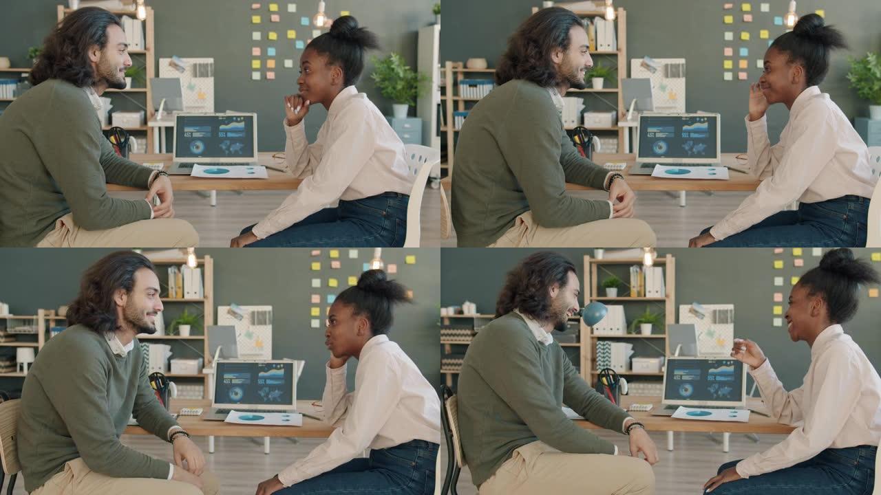 阿拉伯男人和美国黑人女孩在办公室里看着笔记本电脑屏幕聊天和笑