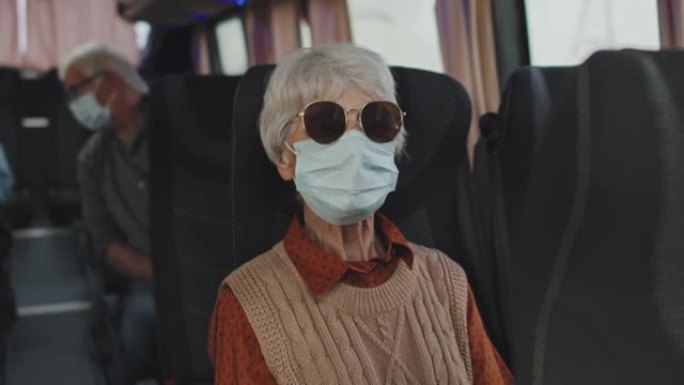 公共汽车上戴着口罩和太阳镜的高级女性