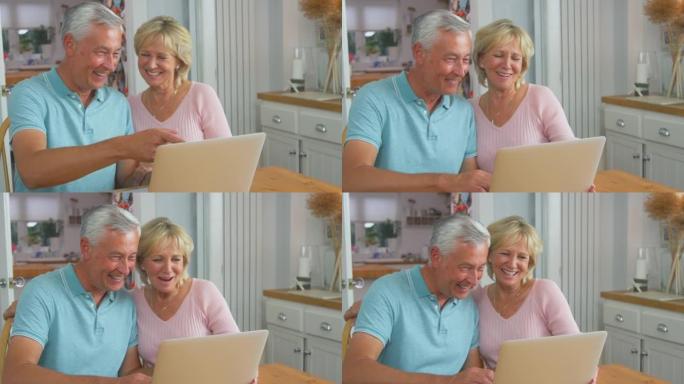 资深退休夫妇坐在家里的桌子旁，用笔记本电脑进行视频通话