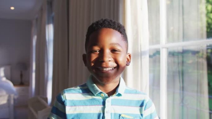 快乐的非洲裔美国男孩的肖像从阳光明媚的窗户向外看，转向相机并微笑着