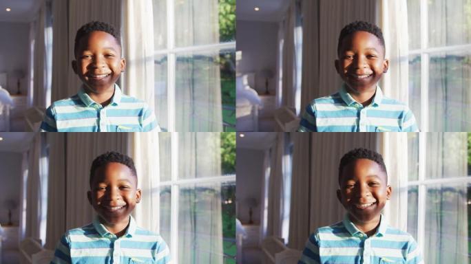 快乐的非洲裔美国男孩的肖像从阳光明媚的窗户向外看，转向相机并微笑着