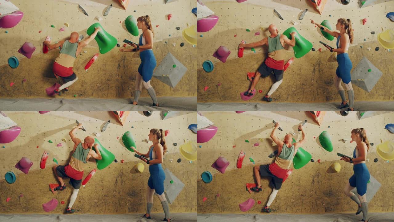 攀岩教练在健身房的抱石墙上给初学者上课。女运动员拿着平板电脑，展示正确的攀爬技术，以强健男性。