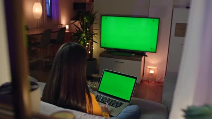 DS年轻女子在家看电视时使用笔记本电脑