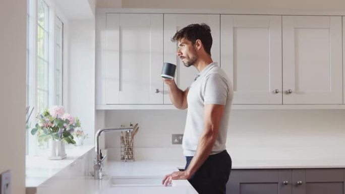 男子站在厨房窗户旁喝热饮放松的早晨镜头