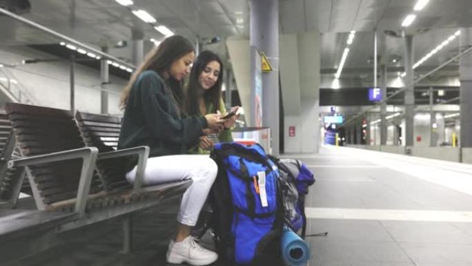 两个女性朋友在车站等铁路，并用手机检查火车时间