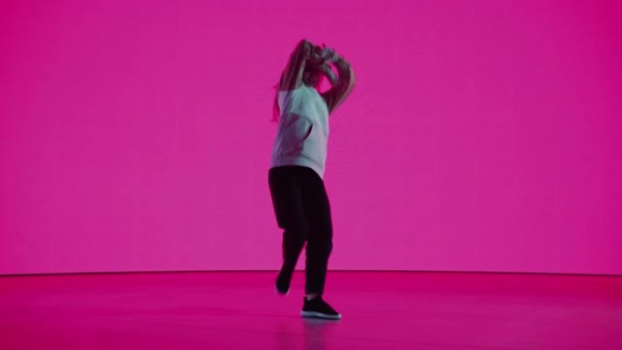 时尚的专业女舞者在工作室环境中的虚拟制作过程中，在具有纯品红色背景的大Led墙屏幕前表演嘻哈舞蹈套路