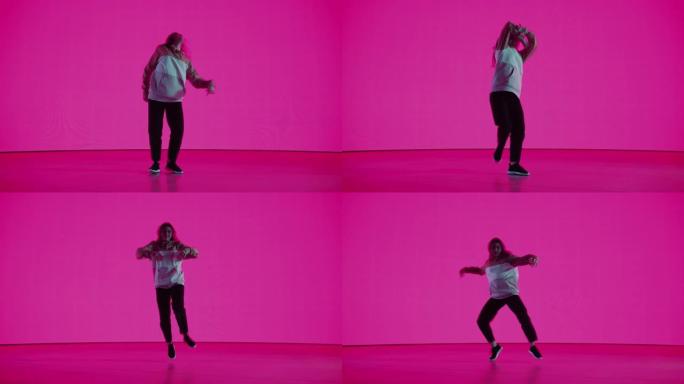 时尚的专业女舞者在工作室环境中的虚拟制作过程中，在具有纯品红色背景的大Led墙屏幕前表演嘻哈舞蹈套路