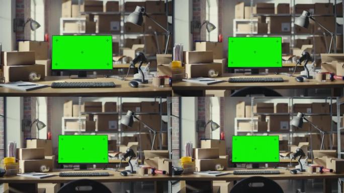 台式计算机显示器站在桌子上，带有绿屏Chromakey模拟显示器。小型企业仓库，工人在后台行走。带纸