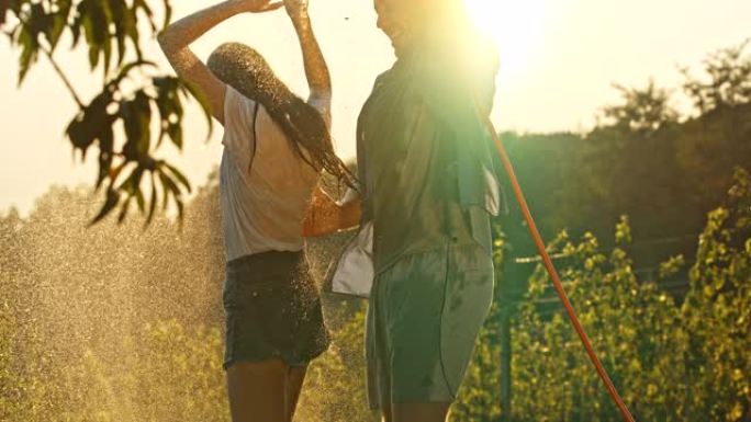 超级SLO MO年轻人玩得开心，用花园软管里的水喷洒他的女朋友