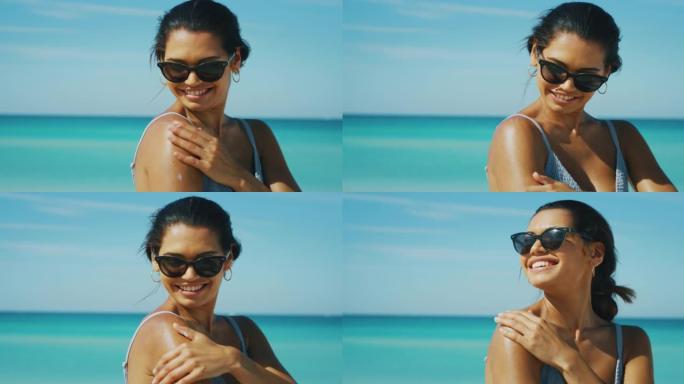 带着太阳镜的快乐年轻黑发女人的慢动作正在海滩度假期间使用防晒霜或晒黑乳液来护理她的皮肤，并在相机中微