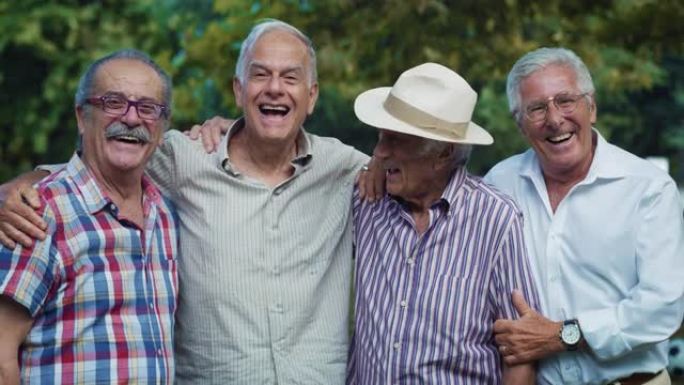 一群微笑而活跃的老人在绿色公园里一起看着相机的肖像。积极的老年朋友摆姿势拍照，以保持他们幸福的团聚记