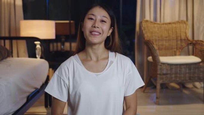 开朗的年轻亚洲女士视频博主晚上在家里客厅的沙发上用手机看着摄像头聊天进行视频直播。