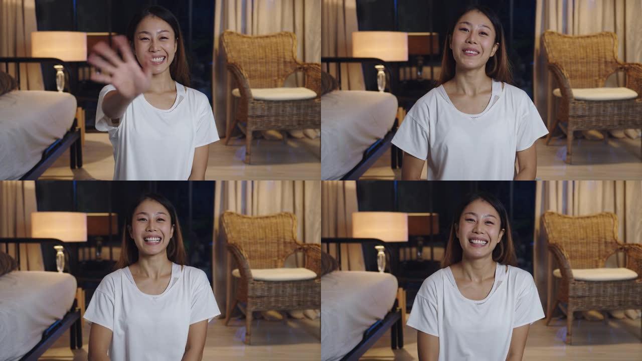 开朗的年轻亚洲女士视频博主晚上在家里客厅的沙发上用手机看着摄像头聊天进行视频直播。