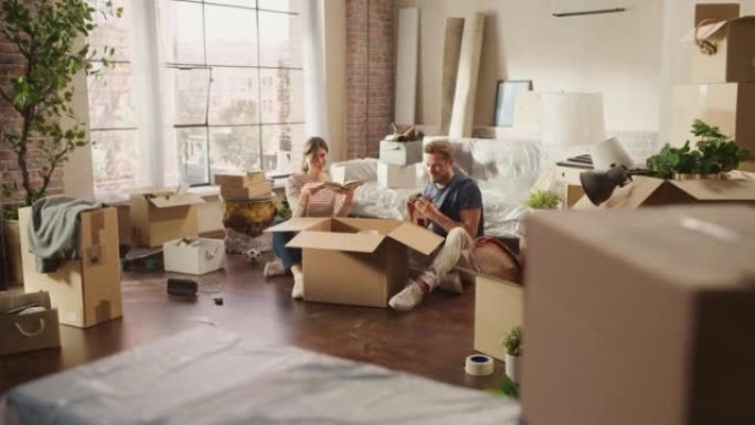 快乐的年轻房主搬进来: 快乐的夫妇坐在新买公寓的地板上打开纸板箱。抵押贷款，房地产，家庭甜蜜之家