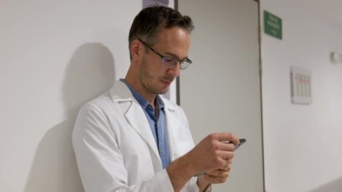 男医生在智能手机上发短信时靠在医院的墙上