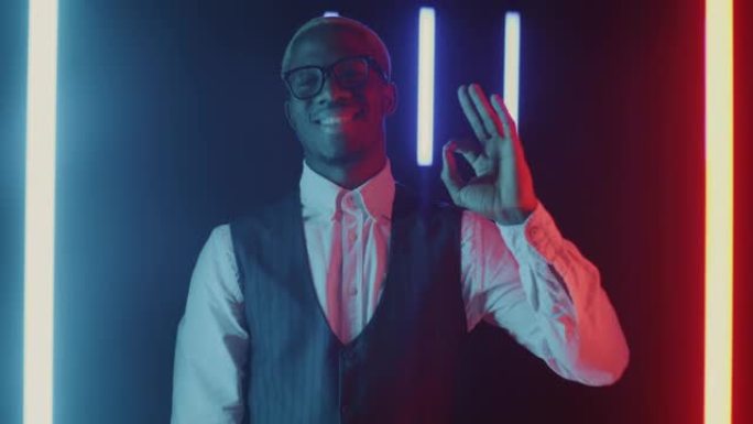 乐观的非洲裔美国商人的慢动作肖像在多色霓虹灯背景上显示OK手势
