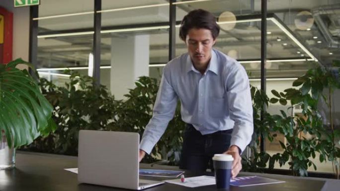 白人商人站在现代办公室中使用笔记本电脑进行文书工作