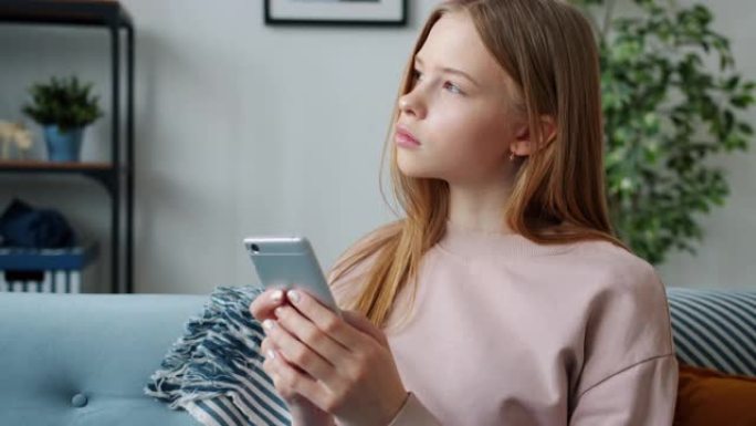 严重的女性青少年使用智能手机发短信坐在公寓的沙发上
