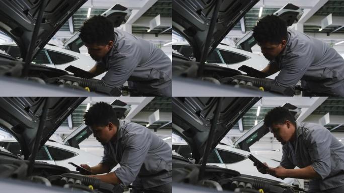 非裔美国男性汽车修理工看着打开的汽车发动机，并使用智能手机