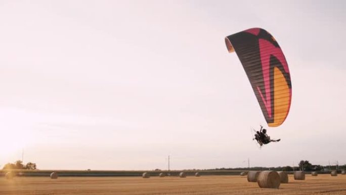 慢动作手持拍摄的滑翔伞飞越装满吨包的收获的农田