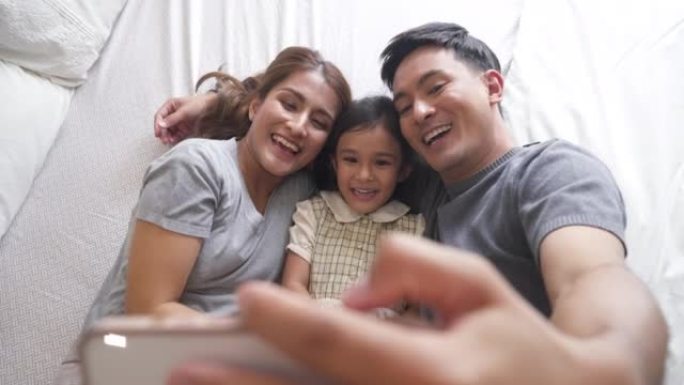 亚洲家庭在床上拥抱，在家中使用电话进行视频通话