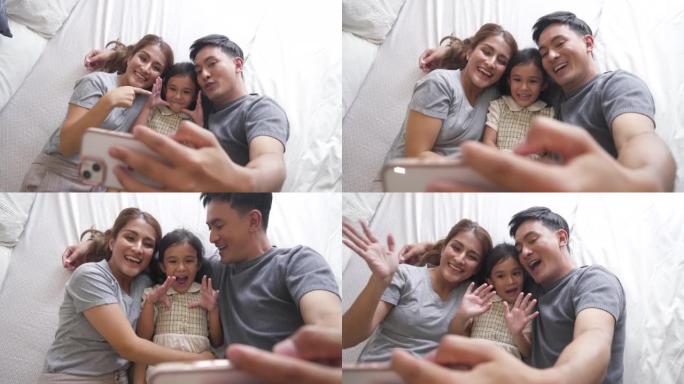 亚洲家庭在床上拥抱，在家中使用电话进行视频通话