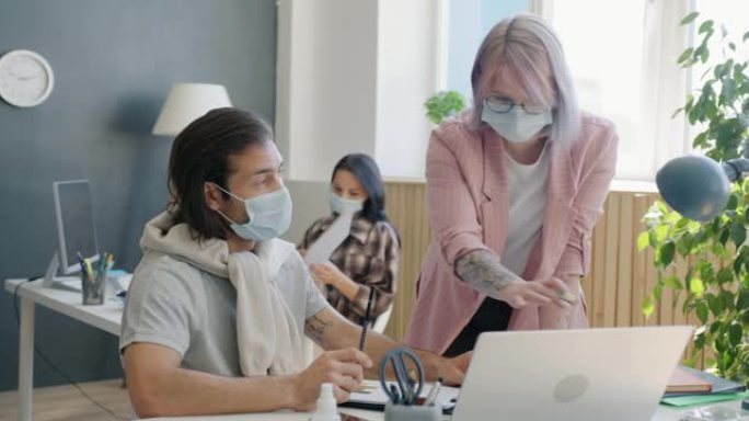 同事男人和女人在办公室里戴着口罩看着笔记本电脑屏幕