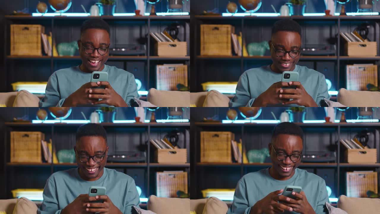 快乐的年轻聪明的黑人男学生在舒适的家中使用智能手机在线玩手机游戏。