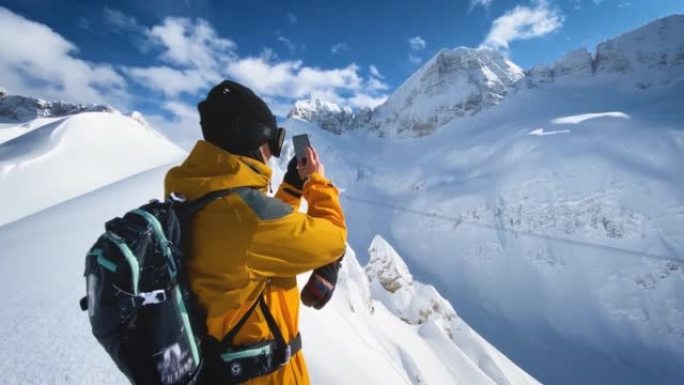 滑雪者在山脊顶上用智能手机拍照