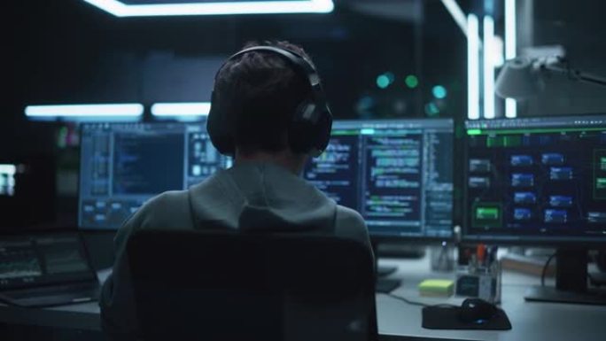 系统管理员在具有多个显示器的计算机上的黑暗研究设施中工作。软件开发人员在休闲服装中戴着耳机并更新服务