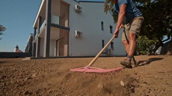 SLO MO房主使用耙子将房屋后面草坪上的土壤夷平