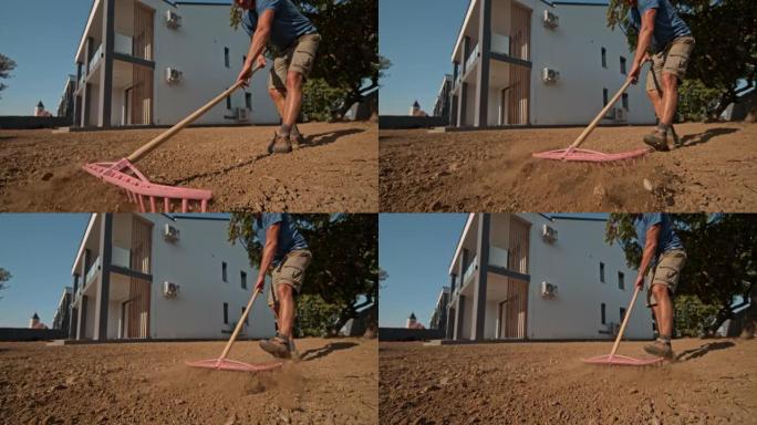 SLO MO房主使用耙子将房屋后面草坪上的土壤夷平