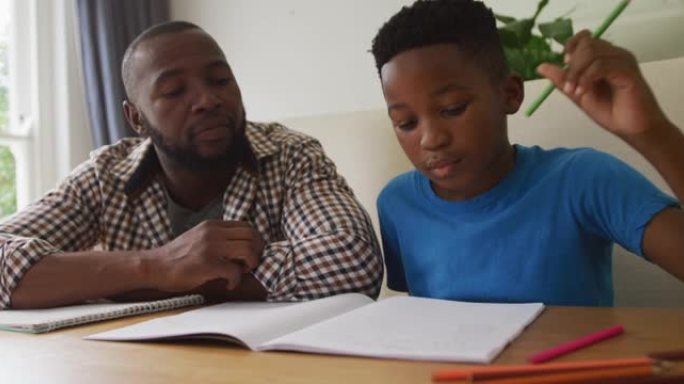 快乐的非洲裔美国父亲坐在厨房的桌子上，帮助儿子完成学业