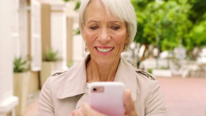 大笑的高级妇女在电话上发短信，浏览社交媒体和互联网。微笑，退休的女士观光并独自站在城市中的顺序。使用