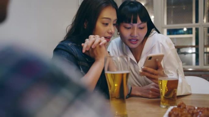 一群快乐的亚洲年轻旅游朋友使用手机，喝酒精啤酒，并在考山路的夜总会举行聚会。