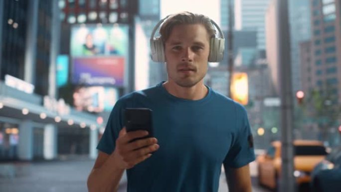 英俊的年轻人在激烈的健身锻炼后走在大城市中心的街道上，并在hid耳机上听音乐时使用智能手机。早上的城